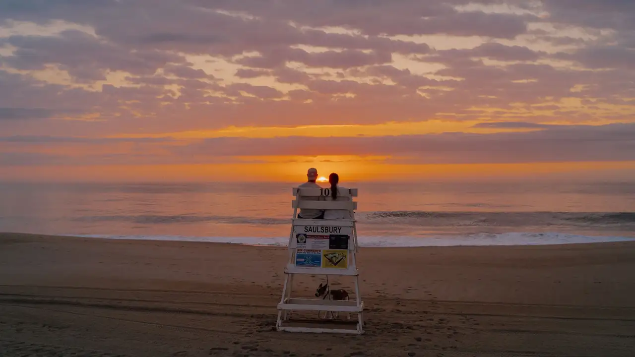 Two people sitting on a lifeguard stand, watching the sun over the ocean.
