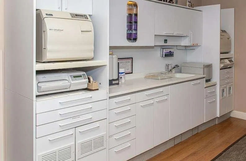 The supply room, with white cabinets and a steriliser on the counter.